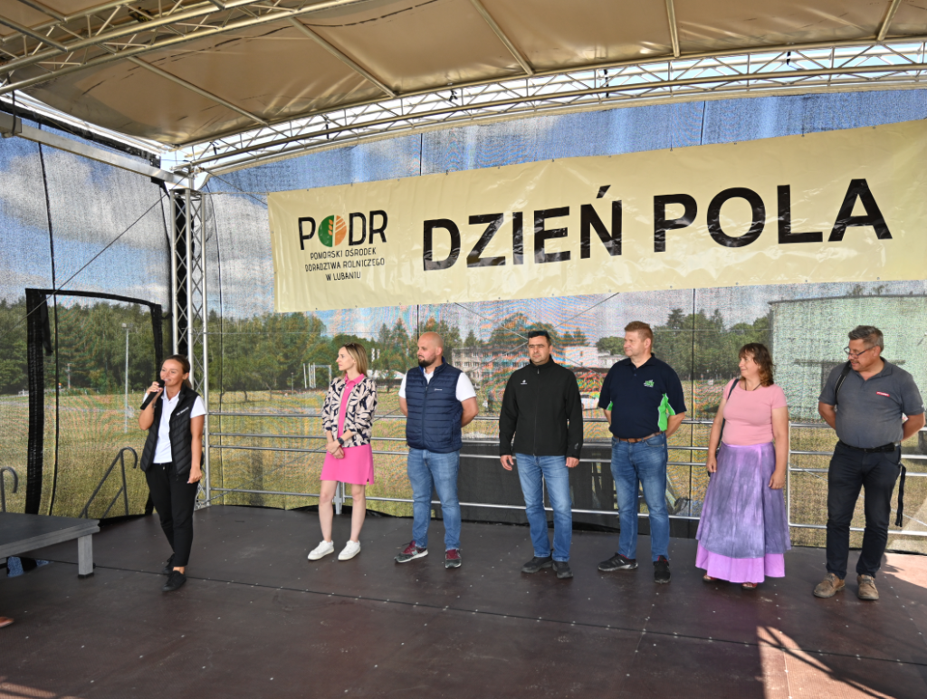 Grupa ekspertów i organizatorów Dnia Pola na scenie podczas prezentacji na tle baneru "Dzień Pola".