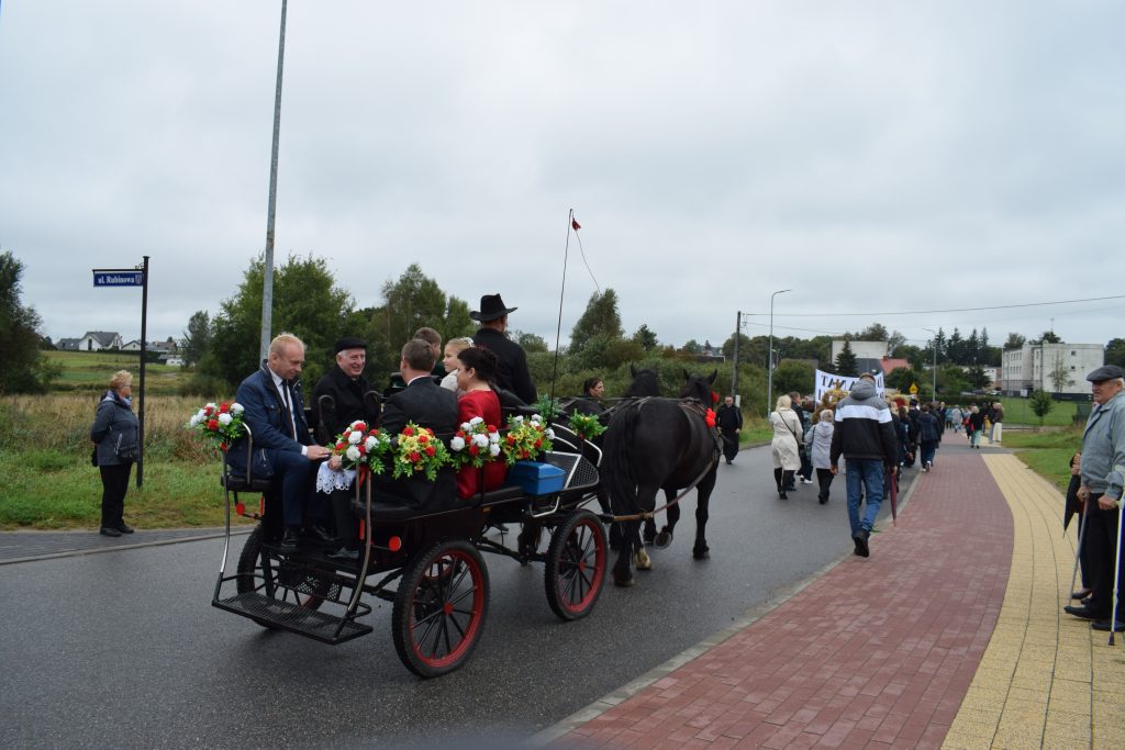 Na zdjęciu widoczna jest bryczka, w której jadą starostowie dożynek wraz z księdzem biskupem Ryszardem Kasyną oraz wójtem gminy Nowa Karczma - Andrzejem Pollakiem. Cała grupa zmierza na uroczystości dożynkowe.