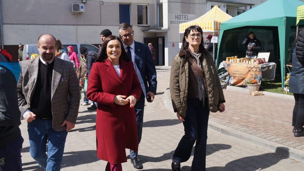 Goście targów spacerują między stoiskami; wśród nich kobieta w czerwonym płaszczu, wokół liczni odwiedzający.