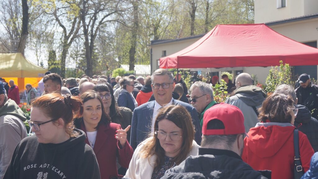 Duża grupa odwiedzający oglądają ofertę i rozmawiają z wystawcami.