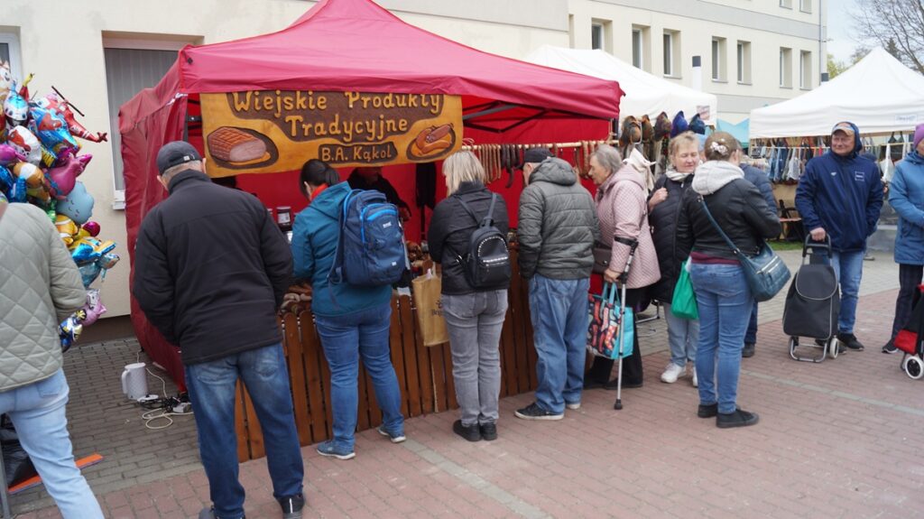 Kolejka do stoiska gastronomicznego pod czerwonym namiotem; uczestnicy targów czekają na zakupy.
