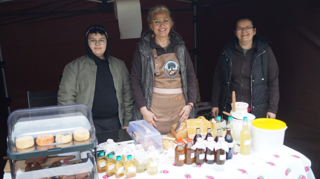 Stoisko Koła Gospodyń Wiejskich; kilka osób stoi za stołem z domowymi produktami i przetworami.