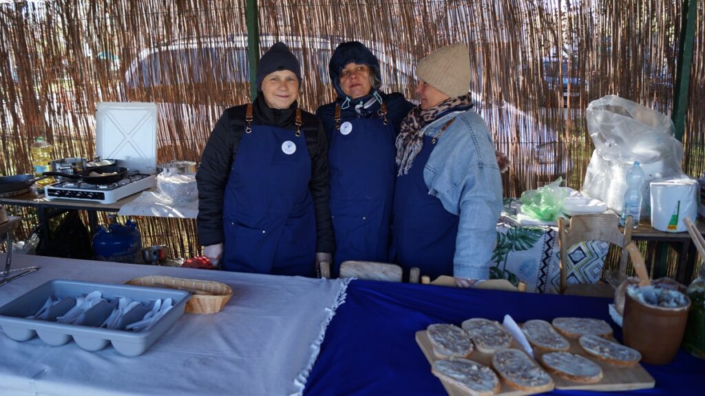Stoisko Koła Gospodyń Wiejskich; kilka osób stoi za stołem z domowymi produktami i przetworami.