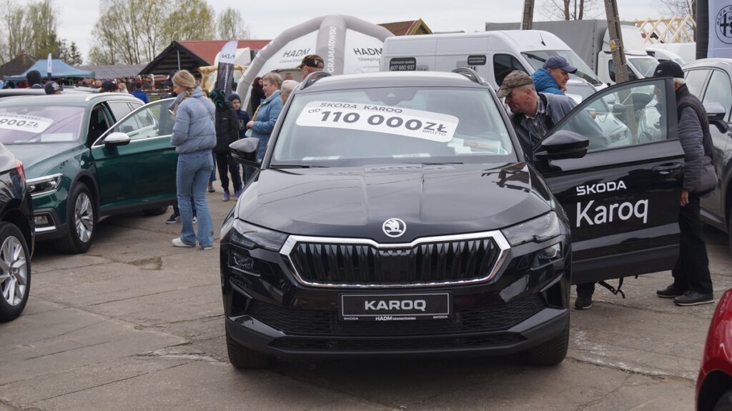 Samochód osobowy prezentowany na stoisku dealerskim; odwiedzający oglądają pojazd.