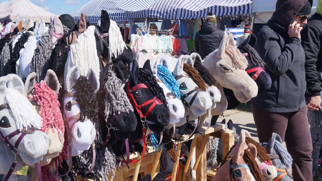 Stoisko z hobby horse – pluszowe głowy koni na kijach zawieszone na ekspozytorach; produkty dla dzieci i młodzieży.