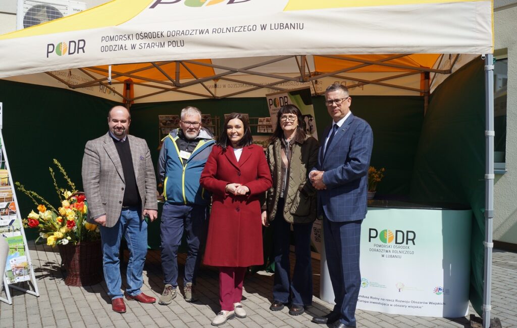 Przedstawiciele PODR i goście stoją przy namiocie z logotypem; wspólne zdjęcie grupowe na tle stoiska.