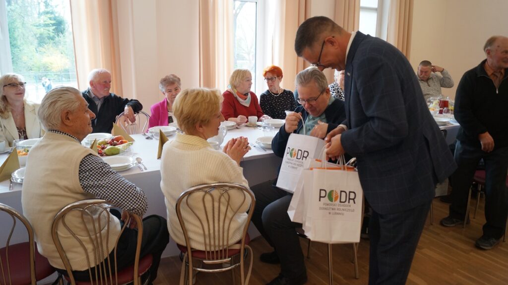 Rozmowy przy stole – uczestnicy spotkania częstują się i integrują podczas wydarzenia. Zastępca dyrektora Adam Klimczak wręcza upominki