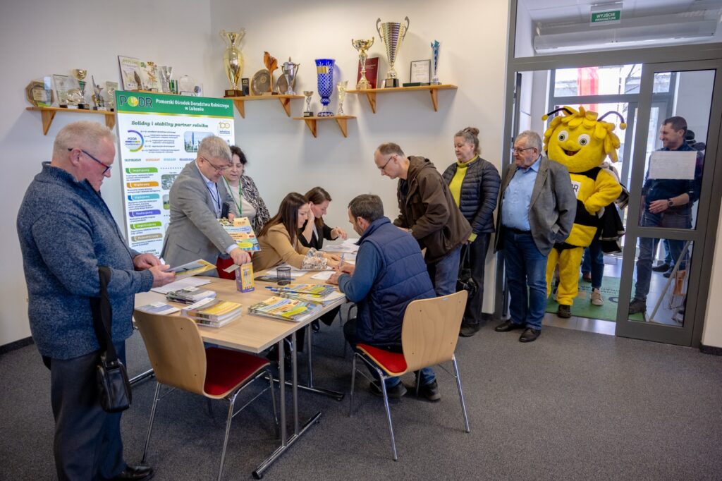 Uczestnicy konferencji przy stole informacyjnym oraz materiały szkoleniowe
