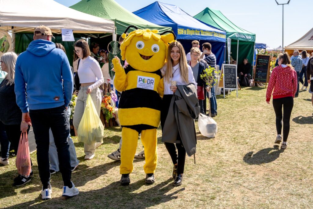 Karolina Wróbel pozująca do wspólnego zdjęcia z maskotką pszczoły wśród odwiedzających targi