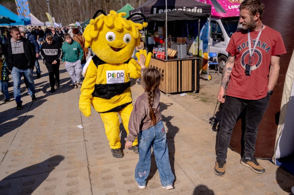 Dziecko tyłem przybijające piątkę z maskotką pszczoły podczas wydarzenia
