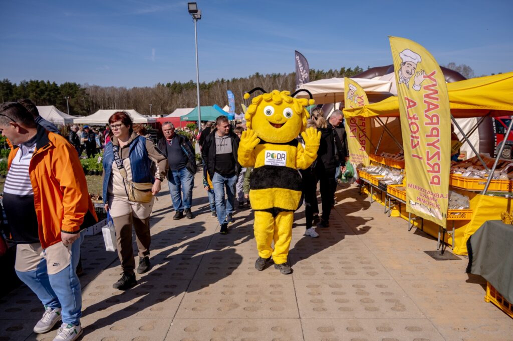 Maskotka pszczoły spacerująca alejką między stoiskami